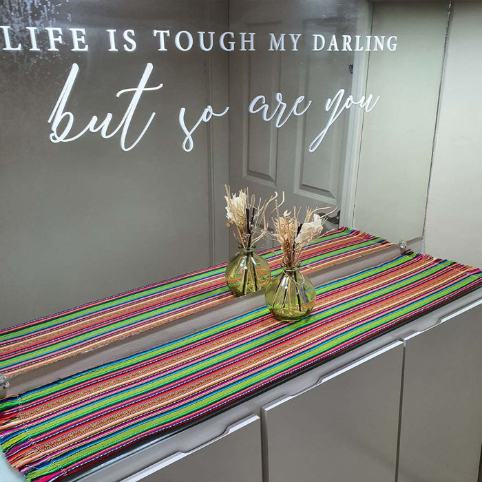 Colorful striped table runner with vases on a kitchen counter, featuring motivational text.