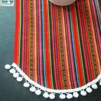 Colorful striped fabric with white pom-pom trim on a dark background