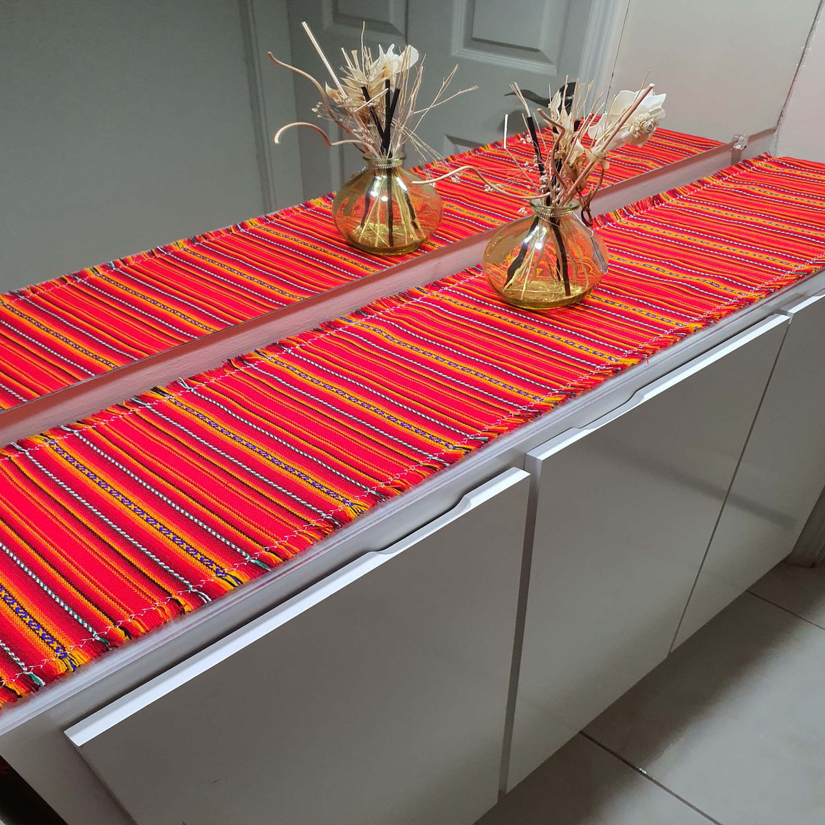 Colorful striped table runner on a white cabinet with decorative vases.