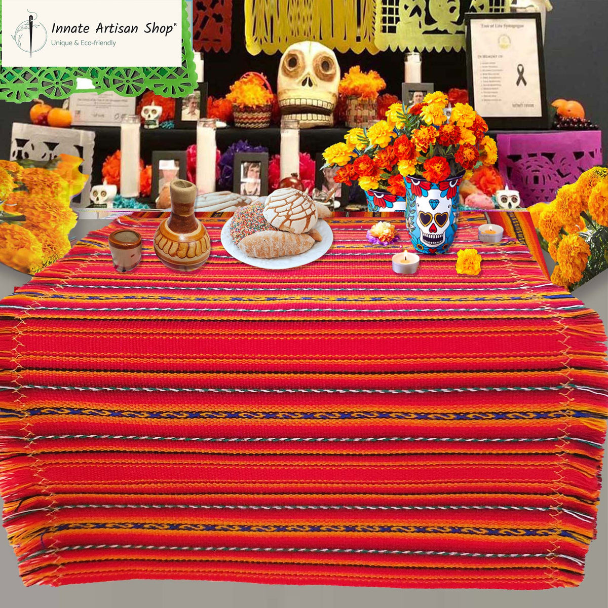 Decorative table setup with colorful tablecloth, flowers, and skull decorations on a gray background.