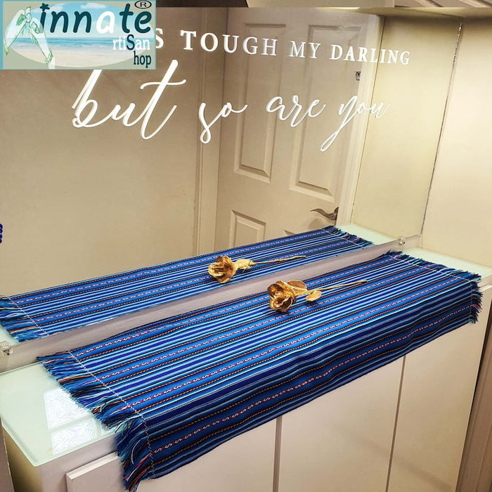 A striped table runner with royal blue as the primary color, featuring multicolored interwoven designs and thin black and white stripes, displayed on a table.