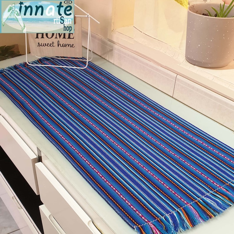 A striped table runner with royal blue as the primary color, featuring multicolored interwoven designs and thin black and white stripes, displayed on a table.