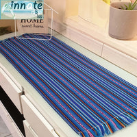 A striped table runner with royal blue as the primary color, featuring multicolored interwoven designs and thin black and white stripes, displayed on a table.