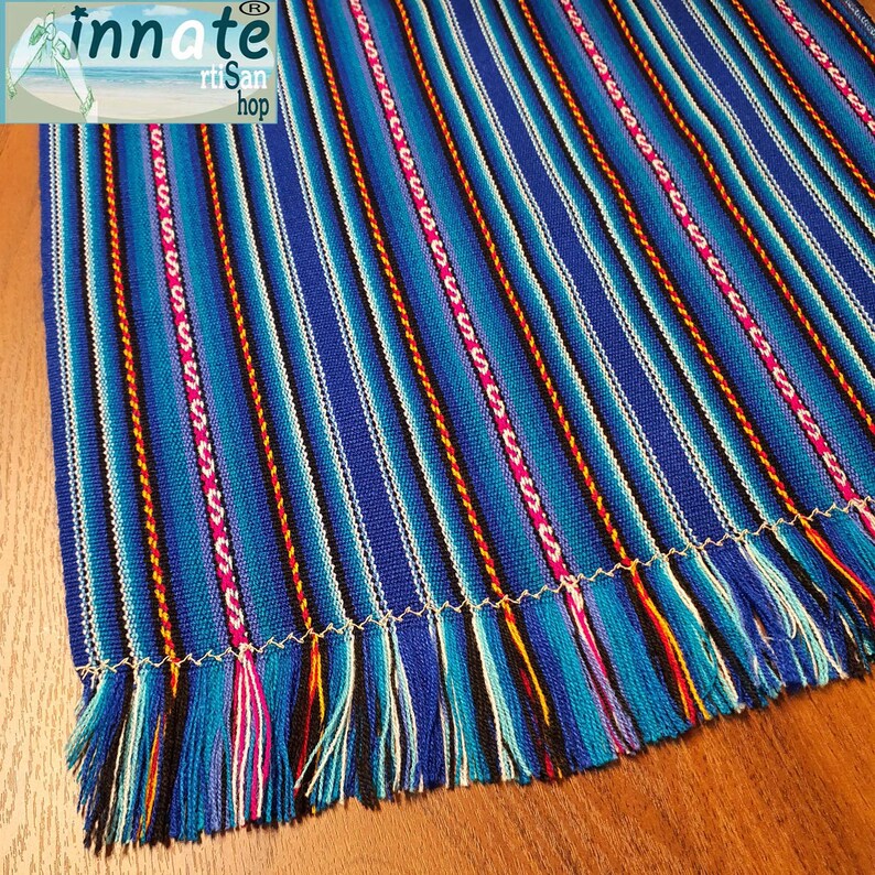 A striped table runner with royal blue as the primary color, featuring multicolored interwoven designs and thin black and white stripes, displayed on a table.