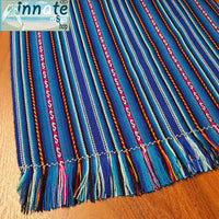 A striped table runner with royal blue as the primary color, featuring multicolored interwoven designs and thin black and white stripes, displayed on a table.