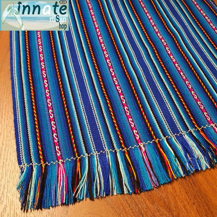 A striped table runner with royal blue as the primary color, featuring multicolored interwoven designs and thin black and white stripes, displayed on a table.